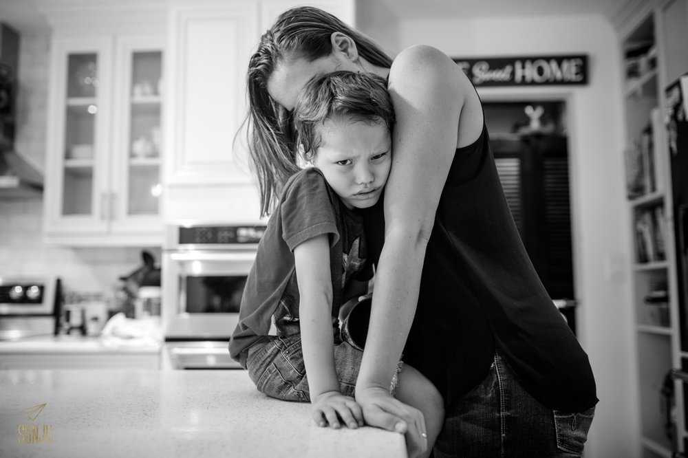  Boy pouts in mom's arms while sitting on kitchen counter&nbsp; 
