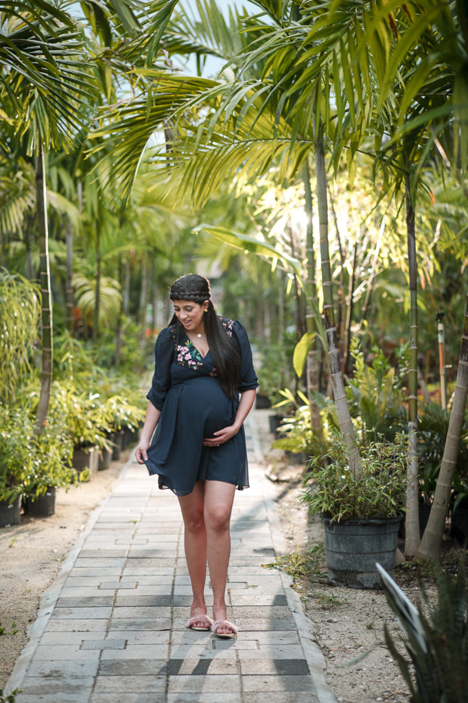 Pregnant woman in short blue dress walks through the nursery at Bamboo Gallery
