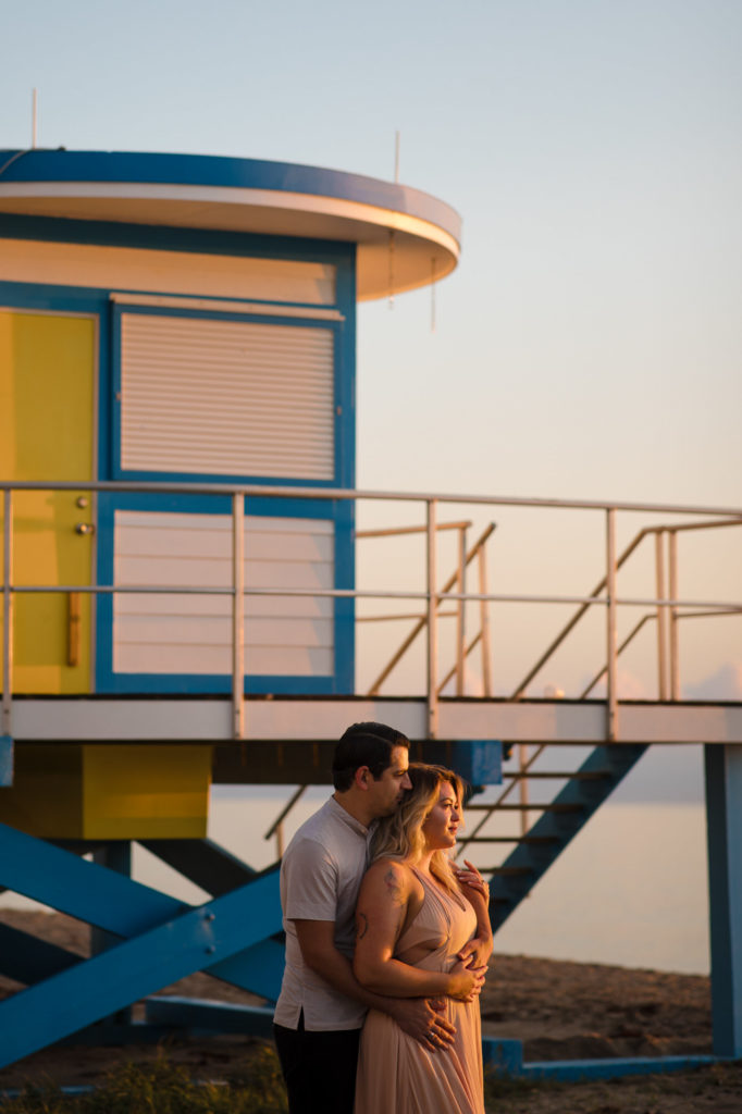 Couple stands next to a lifeguard tower on the beach in Hollywood Florida at sunrise