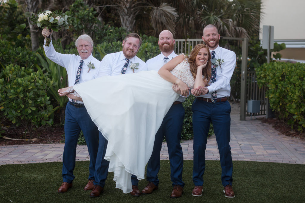 Groomsmen hold up the bride as they pose for a photo