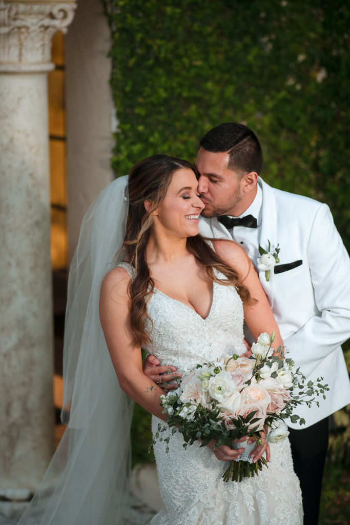groom kisses the cheek of his bride outside the Coral Gables Country Club