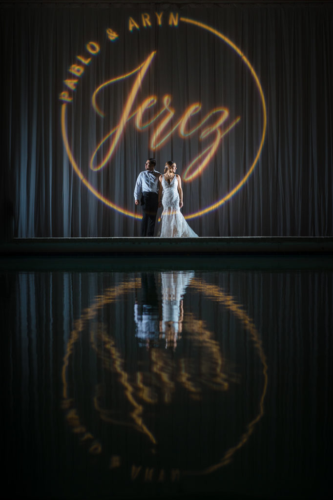 Bride and groom pose in front of their custom monogram gobo at the pool of the Coral Gables Country Club