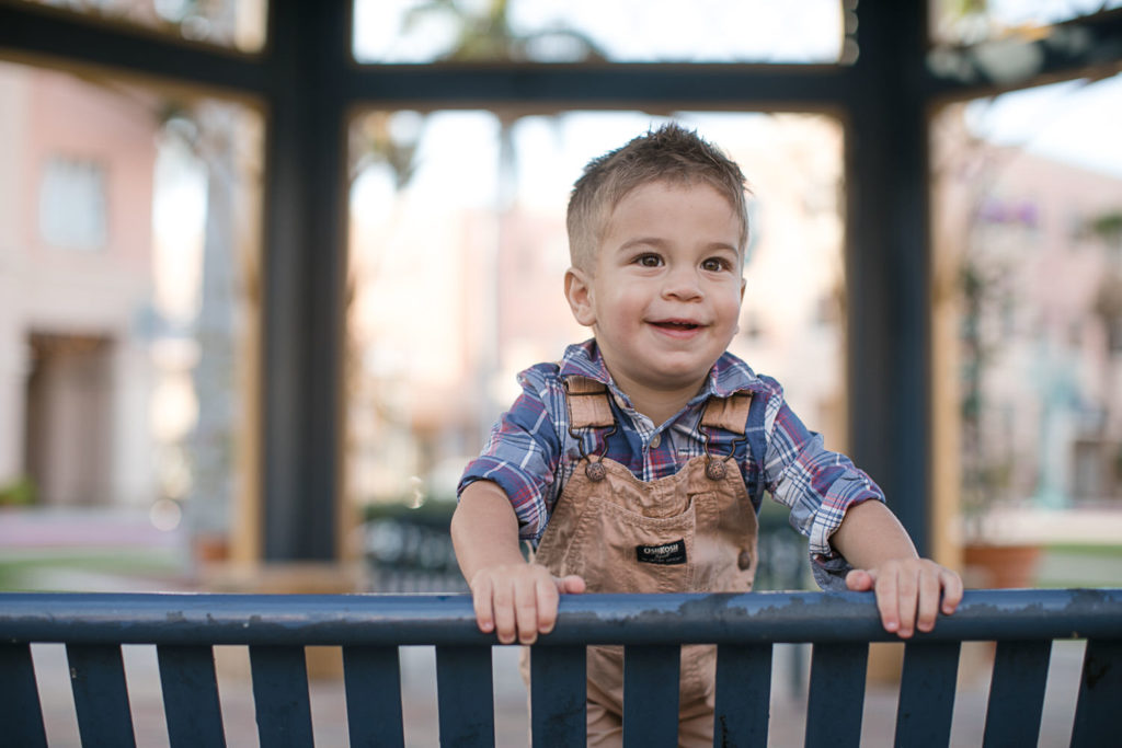 toddler boy looks over a bench at Mizner Park during his family photos session