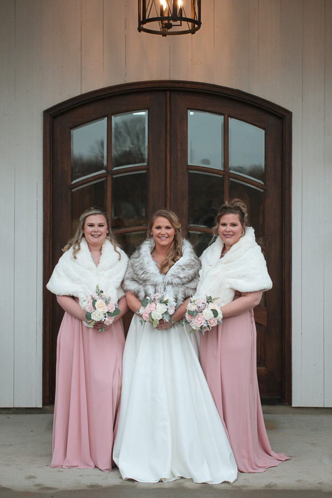 Bride and bridesmaids pose in their pink dresses and faux fur shawls at Chickadee Hill Farms