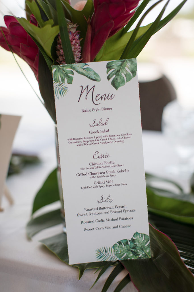 Tropical inspired wedding reception menu leaning against a centerpiece