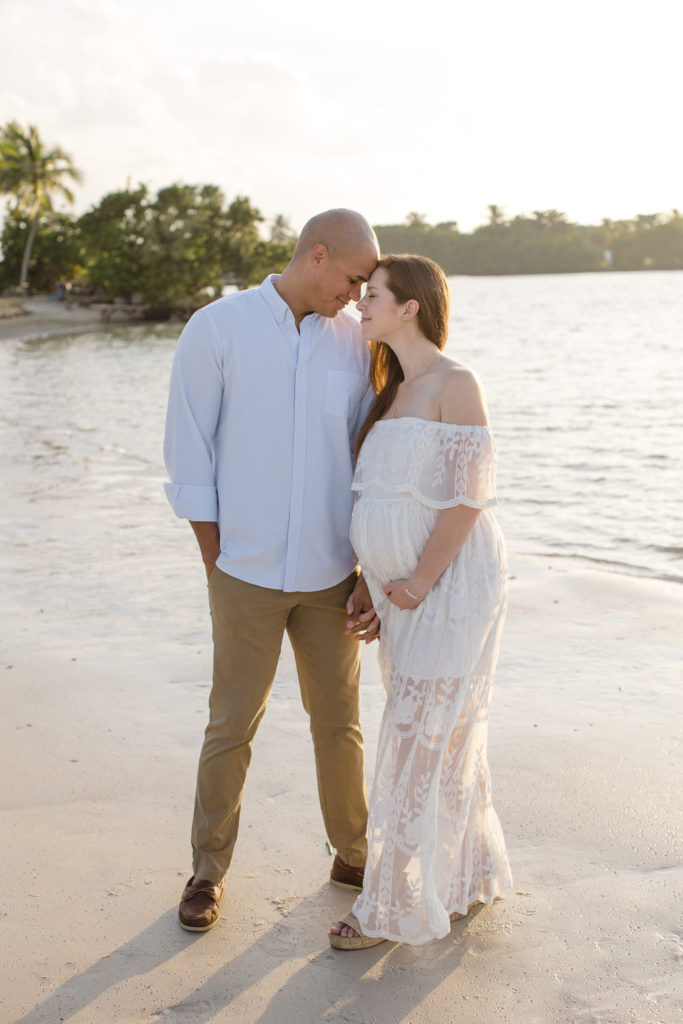 Miami maternity photos featuring a young expecting mom wearing a white lace maternity gown on the beach with her husband