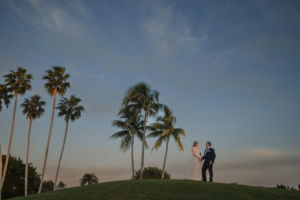 Newlywed couple poses on top of a hill with palm trees at the Westchester Country Club